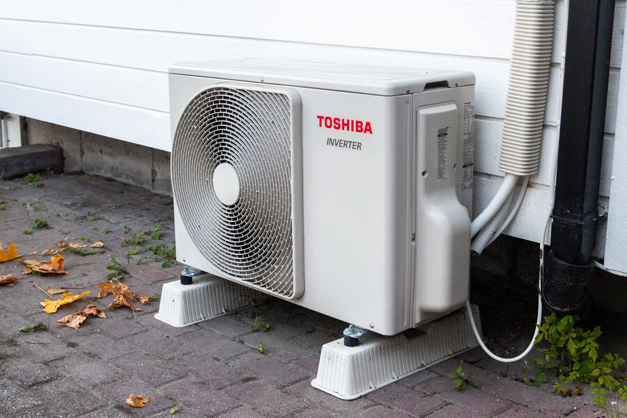 An outdoor heat pump unit on blocks beside a white house