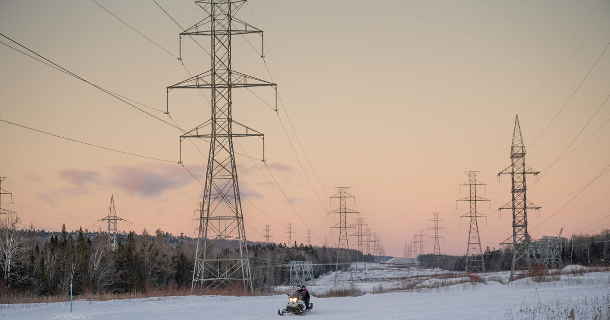 Hydro-Qu&eacute;bec transmission pylons crossing snowy ground at sunset, a snowmobiler riding beneath the lines