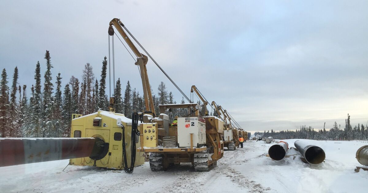 A pipeline crew with sidebooms and lengths of pipe on a snowy right-of-way in the boreal forest