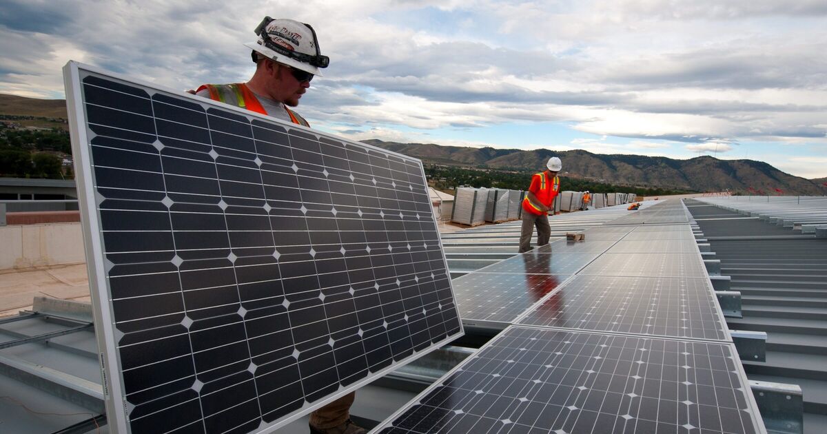 Two solar installers in hard hats fitting a panel into a rooftop array