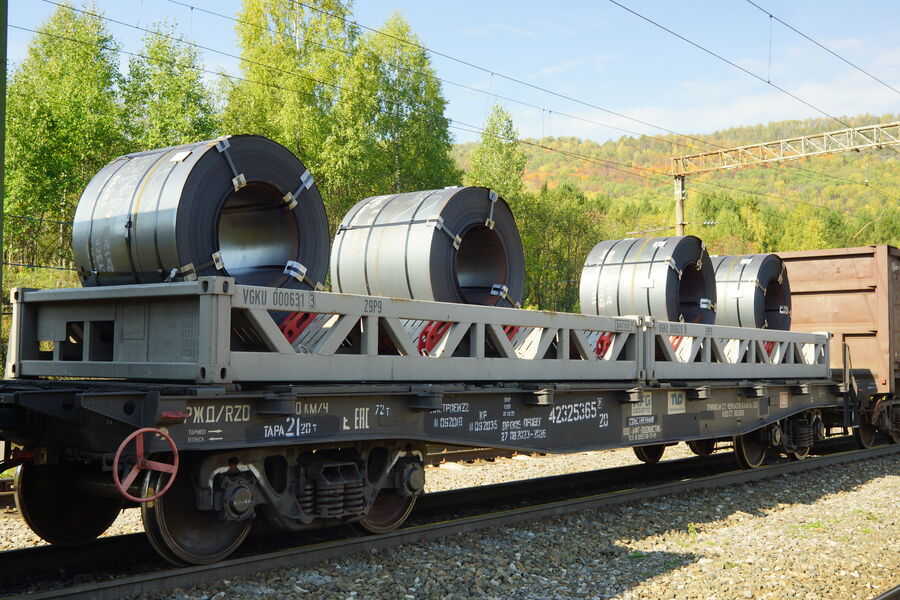 Coils of rolled steel loaded on a flatcar, with green trees behind