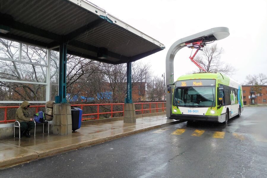A Montreal transit bus charging under an overhead pantograph at a bus terminus